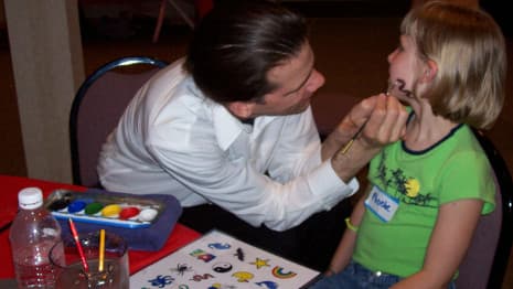 Magician face painting a design on a girl's cheek at a Chicago area event!